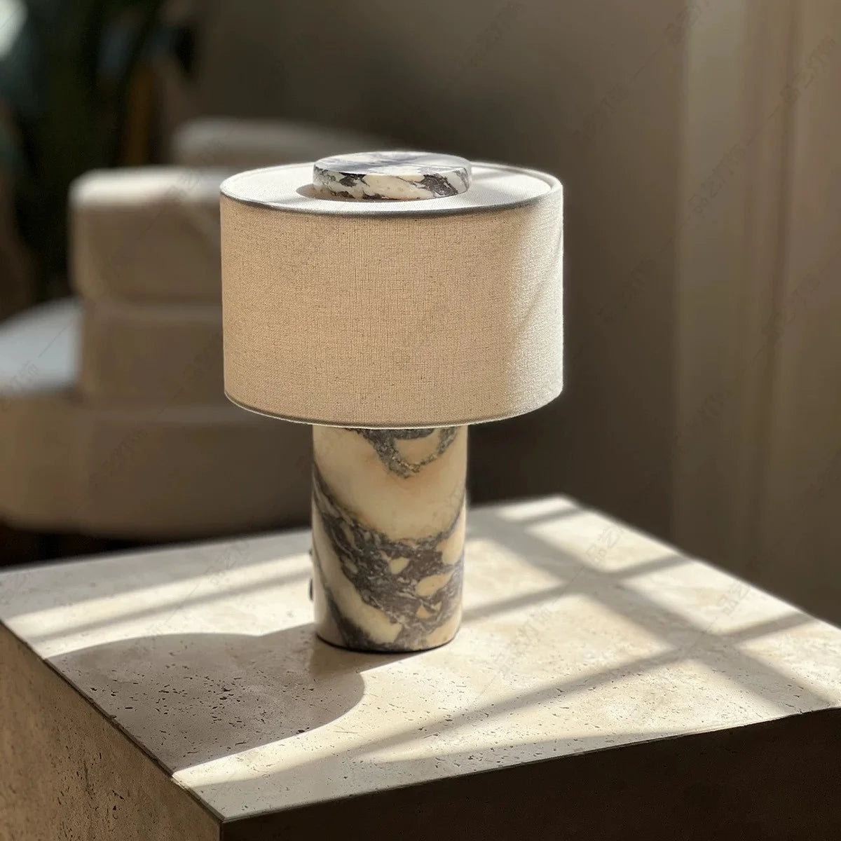 Lampe Isaure en marbre Calacatta Viola posée sur une table de chevet en pierre, lumière chaude du soir