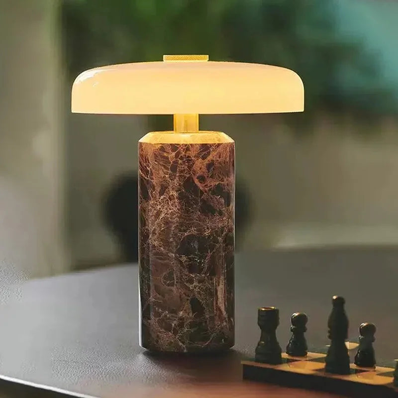 Lampe de chevet sans fil Églantine en marbre rouge, chapeau champignon en verre opalin allumé, posée sur une table