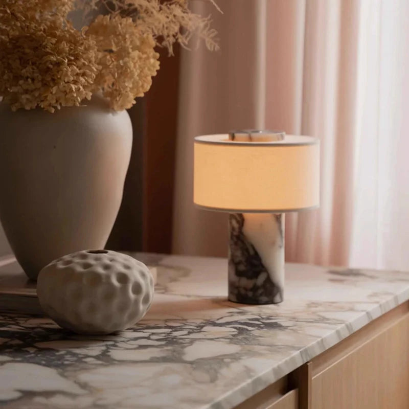 Lampe de table sans fil Isaure sur une console en marbre, à côté d'un vase et d'un bouquet séché