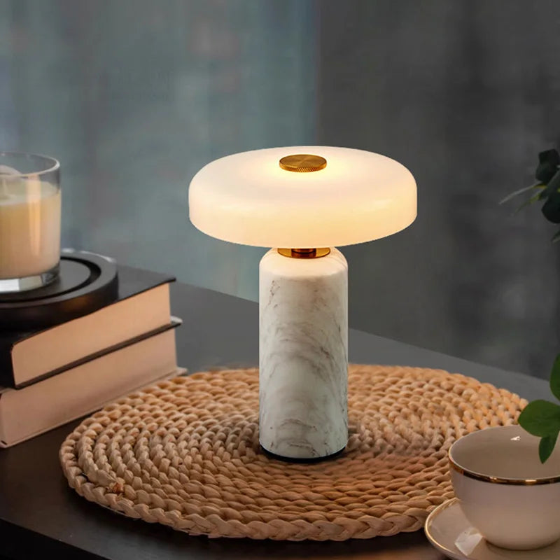 Lampe de chevet sans fil Églantine en marbre blanc allumée sur un set de table en jonc, à côté d'une tasse